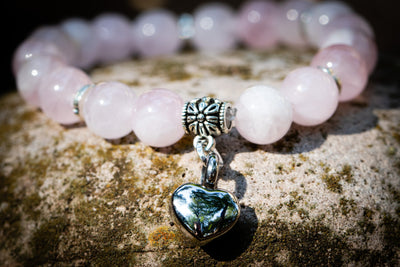 rose quartz beaded bracelet with silver urn heart charm on a textured surface